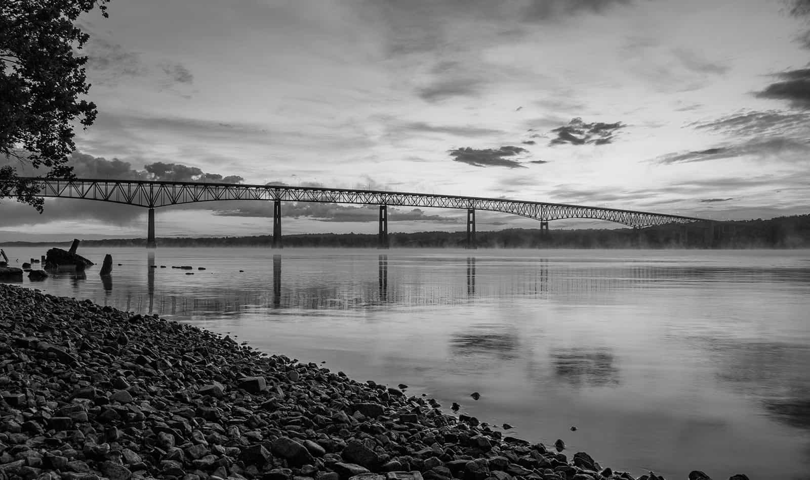 A black and white photo of the Kingston-Rhinecliff Bridge at sunrise.